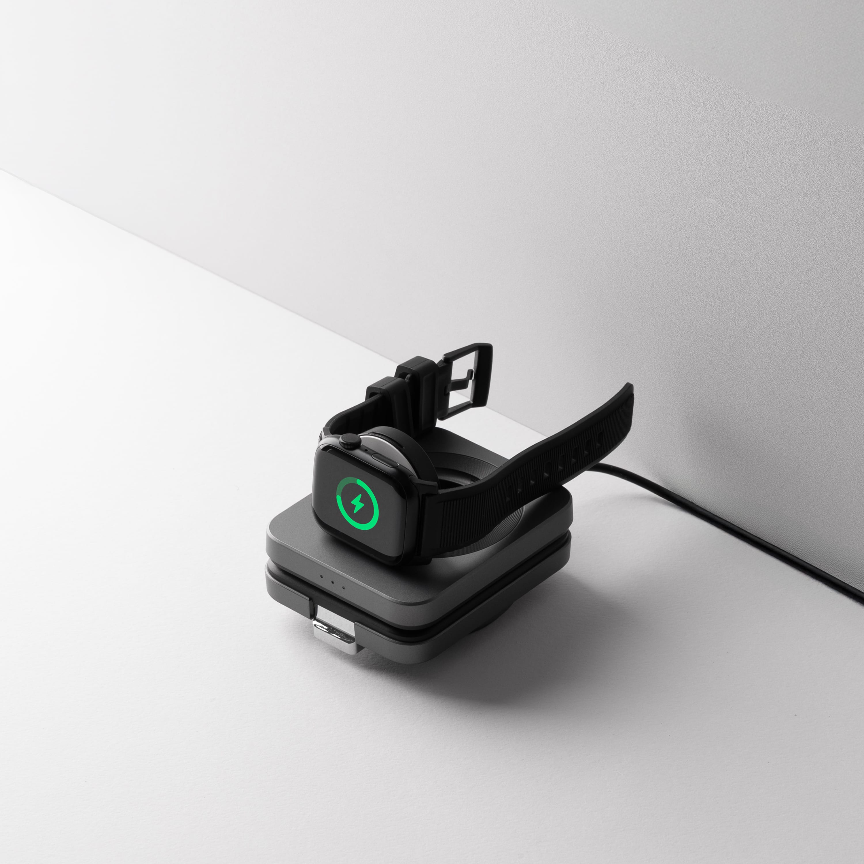 A watch charging on the station's round dock with the green charging bolt lit on its face, the folded panel and its status lights below